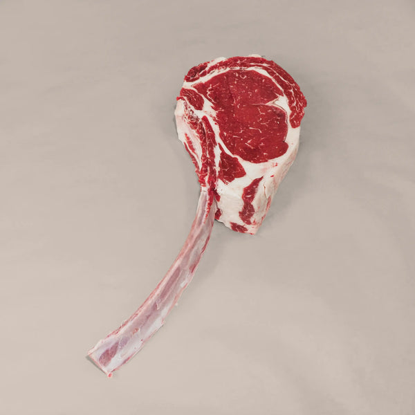 Heavy duty Tomahawk steak with a long bone and marbled texture on a neutral background.
